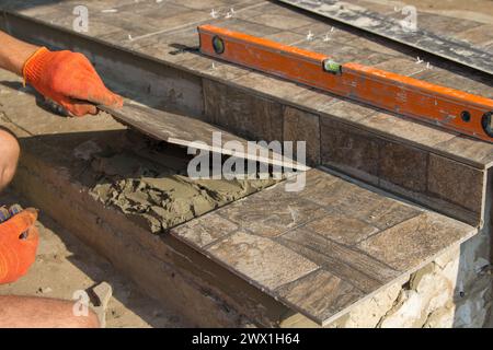 Ein Mann arbeitet als Baumeister, um eine Fliese auf die Treppe des Hauses zu legen Stockfoto