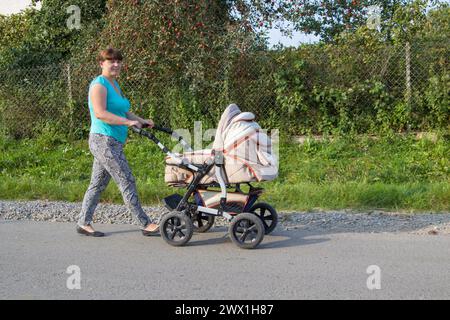 Glückliche Mutter, die einen Kinderwagen fährt, ein neugeborenes Baby im Sommer auf der Straße Stockfoto