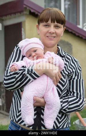 Im Hof neben dem Haus hält eine Frau ein Baby in den Armen Stockfoto