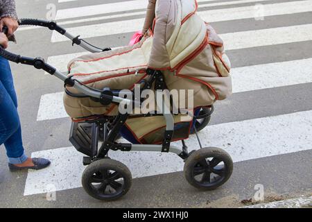 Frau auf der Straße schiebt einen alten Kinderwagen auf die Straße Stockfoto