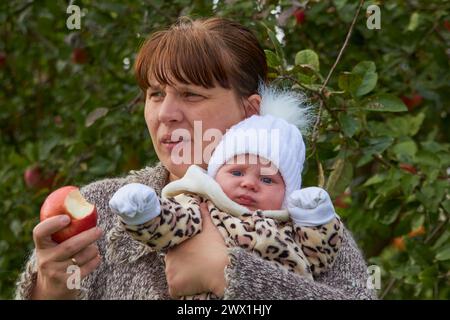 Im Herbstgarten isst eine Mutter mit einem Baby einen Apfel Stockfoto