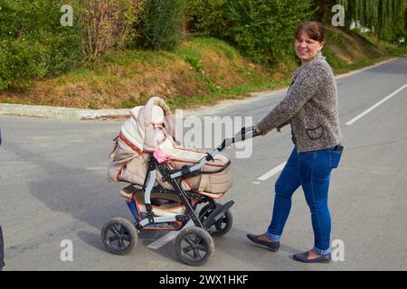 Mama mit Kinderwagen überquert die Straße im Dorf Stockfoto