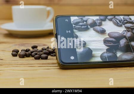 Nahaufnahme eines Smartphones, das ein Foto verschütteter Kaffeebohnen auf einem Tisch in einem Café macht Stockfoto