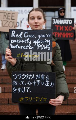 Ukrainische Aktivistin posiert mit dem Banner "Rotes Kreuz, du genehmigst Passiv Folterungen an Kriegsgefangenen" in englischer und japanischer Sprache bei einer öffentlichen Demonstration. Kiew - 24. März 2024 Stockfoto