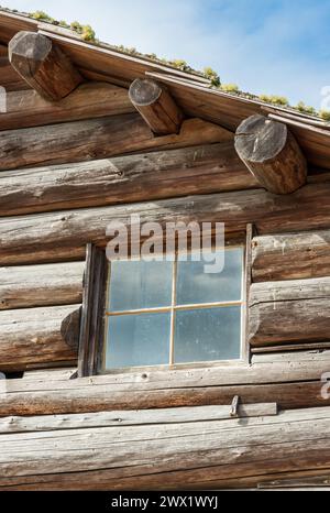 Ein kleines Fenster mit Glasverkleidung sitzt in grob behauenen Stämmen unter einem moosigen Dachrand im Ebey's Landing National Historical Reserve, Washington. Stockfoto