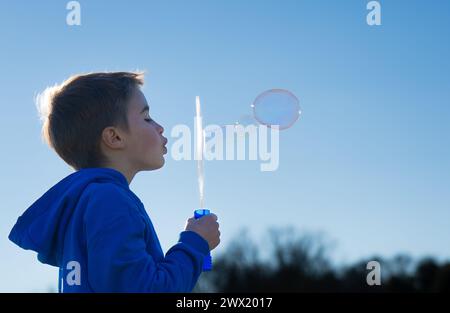 Kind bläst Seifenblasen mit einem Bubbler mit blauem Himmel im Hintergrund Stockfoto