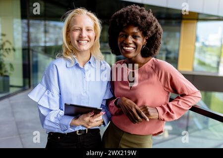 Zwei Frauen mit ähnlichen Merkmalen stehen nebeneinander, lächelnd, vor der großen Architektur. Stockfoto