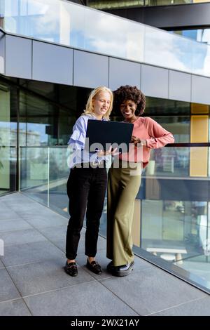 Zwei Frauen mit ähnlichen Merkmalen stehen nebeneinander, lächelnd, vor der großen Architektur. Stockfoto