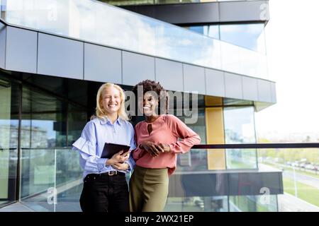 Zwei Frauen mit ähnlichen Merkmalen stehen nebeneinander, lächelnd, vor der großen Architektur. Stockfoto