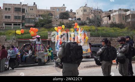 Jüdische Siedler in Kostümen tanzen während der jährlichen Purim-Parade, während israelische Sicherheitskräfte die Feierlichkeiten am 24. März 2024 in Hebron sichern. Stockfoto