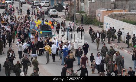 Jüdische Siedler in Kostümen tanzen während der jährlichen Purim-Parade, während israelische Sicherheitskräfte die Feierlichkeiten am 24. März 2024 in Hebron sichern. Stockfoto