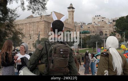 Jüdische Siedler in Kostümen tanzen während der jährlichen Purim-Parade, während israelische Sicherheitskräfte die Feierlichkeiten am 24. März 2024 in Hebron sichern. Stockfoto