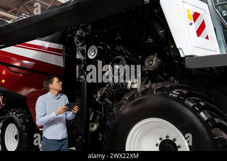 Servicemitarbeiter mit digitalem Tablet auf einem neben Ombinen-Harvester mit offener Haube. Stockfoto