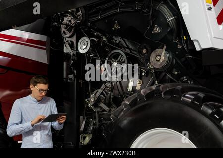 Servicemitarbeiter mit digitalem Tablet auf einem neben Ombinen-Harvester mit offener Haube. Stockfoto