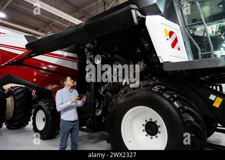 Servicemitarbeiter mit digitalem Tablet auf einem neben Ombinen-Harvester mit offener Haube. Stockfoto