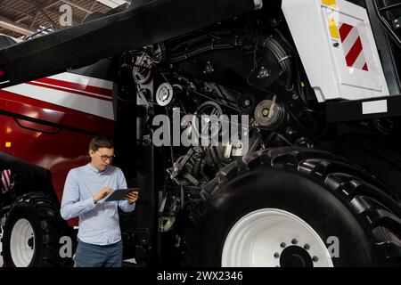 Servicemitarbeiter mit digitalem Tablet auf einem neben Ombinen-Harvester mit offener Haube. Stockfoto