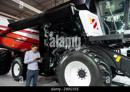 Servicemitarbeiter mit digitalem Tablet auf einem neben Ombinen-Harvester mit offener Haube. Stockfoto