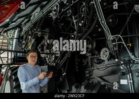 Servicemitarbeiter mit digitalem Tablet auf einem neben Ombinen-Harvester mit offener Haube. Stockfoto