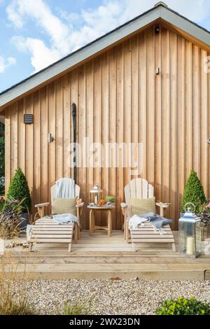 Hölzerne Liegestühle auf einer hölzernen Terrasse im Garten eines hölzernen Ferienhauses in Suffolk, Großbritannien Stockfoto