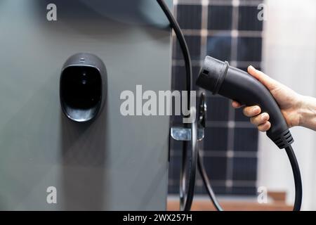 Hand mit Elektrofahrzeug-Ladestecker auf einem Hintergrund des Solarmoduls. Stockfoto