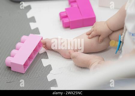 Das Kind greift während des Sitzens spielerisch mit Blöcken und anderen Spielzeugen in der Kinderbetreuung um. Enge Feldtiefe bei Nahaufnahmen der Hände des Neugeborenen Stockfoto