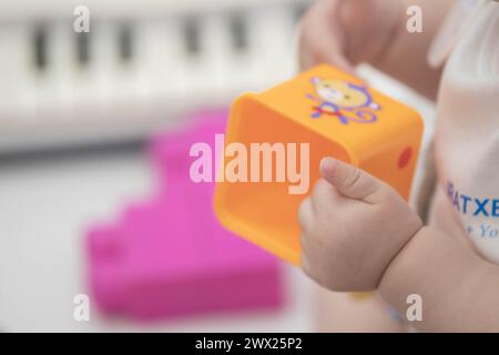 Das Kind greift während des Sitzens spielerisch mit Blöcken und anderen Spielzeugen in der Kinderbetreuung um. Enge Feldtiefe bei Nahaufnahmen der Hände des Neugeborenen Stockfoto