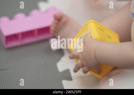 Das Kind greift während des Sitzens spielerisch mit Blöcken und anderen Spielzeugen in der Kinderbetreuung um. Enge Feldtiefe bei Nahaufnahmen der Hände des Neugeborenen Stockfoto