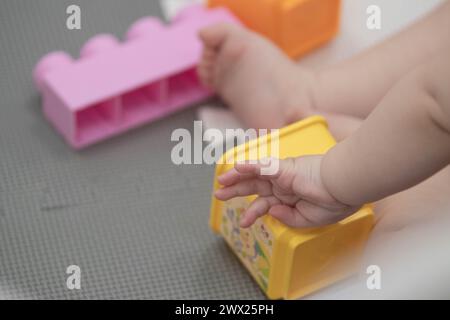 Das Kind greift während des Sitzens spielerisch mit Blöcken und anderen Spielzeugen in der Kinderbetreuung um. Enge Feldtiefe bei Nahaufnahmen der Hände des Neugeborenen Stockfoto