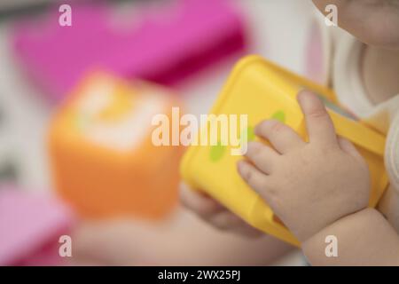 Das Kind greift während des Sitzens spielerisch mit Blöcken und anderen Spielzeugen in der Kinderbetreuung um. Enge Feldtiefe bei Nahaufnahmen der Hände des Neugeborenen Stockfoto