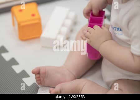 Das Kind greift während des Sitzens spielerisch mit Blöcken und anderen Spielzeugen in der Kinderbetreuung um. Enge Feldtiefe bei Nahaufnahmen der Hände des Neugeborenen Stockfoto