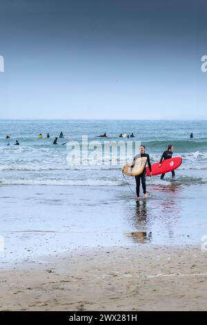 Surferinnen, die ihre Surfbretter tragen und am Towan Beach in Newquay im britischen Cornwall aus dem Meer spazieren. Stockfoto