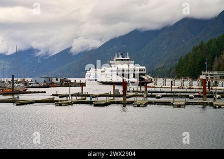 Zwei BC-Fähren verlassen den Fährhafen Horseshoe Bay mit grünen Bergen und dramatischen Wolken im Hintergrund am Tag Stockfoto