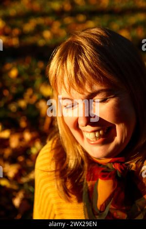 Porträt einer fröhlichen Frau mit strahlendem Lächeln, die die Herbststimmung im Park genießt, perfekt für Lifestyle-Magazine, Herbstwerbung Stockfoto