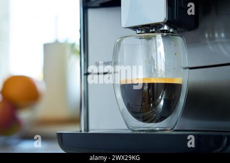 Frischer Espresso in klarem Glas am Morgen. Kaffeemaschine in der Küche, Nahaufnahme. Moderne Kaffeemaschine mit frisch gebrühtem Kaffee in Glasbecher. Küchengeräte Stockfoto