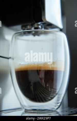 Frischer Espresso in klarem Glas am Morgen. Kaffeemaschine auf dunklem Hintergrund, Nahaufnahme. Moderne Kaffeemaschine mit frisch gebrühtem Kaffee in Glasbecher. Ki Stockfoto