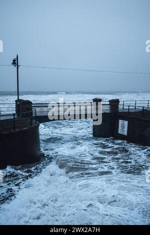 Flut am Meer in der Stadt Filey an der Yorkshire Coast in England, mit Wellen, die unter der Brücke über die Slipway zum Strand fließen. Stockfoto