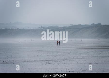 Ein Paar zu Fuß in der Ferne am Sandstrand von Filey Bay an der wunderschönen Yorkshire Coast in England bei Ebbe. An einem bewölkten Tag. Stockfoto