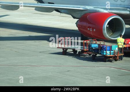 Gepäckabfertigung am Flughafen mit Anhänger, der Koffer zwischen Flughafenterminal und Flugzeug transportiert Stockfoto