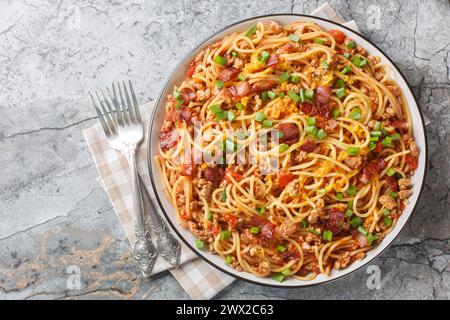 Köstliche Spaghetti mit Speck, Hackfleisch, Cheddar-Käse, Zwiebeln und scharfer Tomatensoße in Nahaufnahme auf einem Teller auf dem Tisch. Horizontale Draufsicht von einem Stockfoto