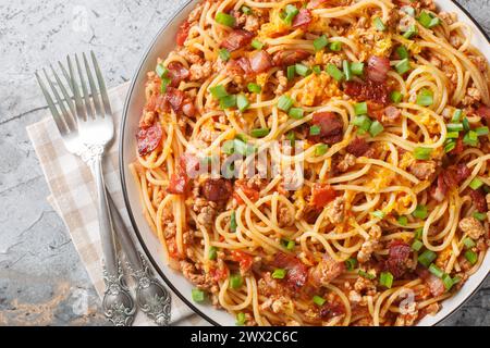 Amerikanische Spaghetti mit Speck, Hackfleisch, Cheddar-Käse und scharfer Tomatensauce in Nahaufnahme auf einem Teller auf dem Tisch. Horizontale Draufsicht von oben Stockfoto