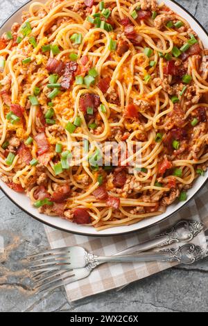 Amerikanische Spaghetti-Pasta mit Speck, Hackfleisch, Cheddar-Käse, Zwiebeln und scharfer Tomatensauce in Nahaufnahme auf einem Teller auf dem Tisch. Vertikal oben VI Stockfoto
