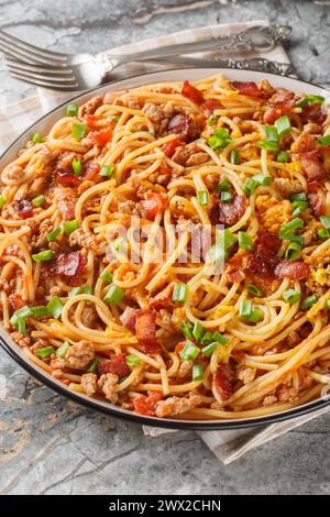 Cowboy-Spaghetti mit Hackfleisch, Speck, Cheddar-Käse, Zwiebeln, Pfeffer und Tomaten aus der Nähe auf dem Teller auf dem Tisch. Vertikal Stockfoto