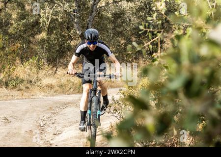 Vorderansicht eines jungen erwachsenen Mountainbikers, der einen Trail in einem Wald hinauffährt. Stockfoto