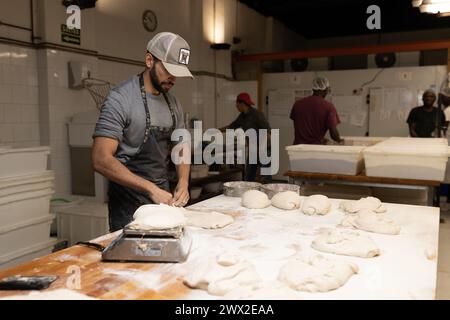 Junger erwachsener Bäcker, der Teige zubereitete, um Brot auf dem Bäckereitisch zu machen, die Teige wog, Bäckereischule. Stockfoto