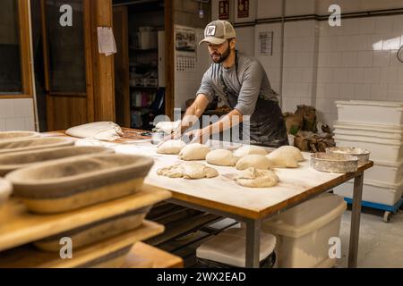 Junger erwachsener Bäcker, der Teige zubereitete, um Brot auf dem Bäckereitisch zu machen, die Teige wog, Bäckereischule. Stockfoto