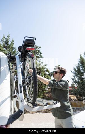 Ein junger Geschäftsmann fährt E-Bike und lädt das Fahrrad auf den Fahrradträger seines Fahrzeugs Stockfoto