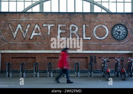 Verblasstes Schild für den Bahnhof Waterloo, da die Menschen am 6. März 2024 in London, Großbritannien, vorbeifahren. Der Bahnhof Waterloo, auch bekannt als London Waterloo, ist ein wichtiger zentraler Endpunkt des National Rail-Netzes im Londoner Stadtteil Lambeth. Es ist mit einer gleichnamigen Londoner U-Bahn-Station verbunden. Waterloo ist der drittgrößte Bahnhof im Vereinigten Königreich, der ab 2023 fast 60 Millionen Passagiere pro Jahr umfasste. Stockfoto