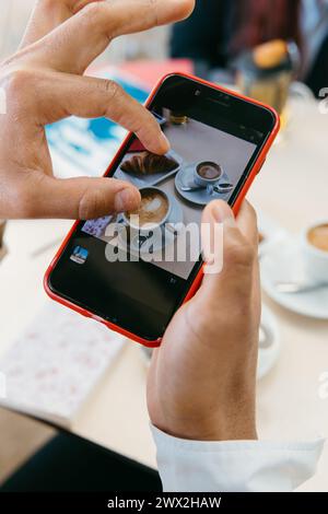 Die Hände bilden ein stilvolles Layout für Kaffeetassen auf einem Smartphone und verkörpern die moderne Kultur der sozialen Medien. Stockfoto