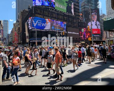 Während der Sommerferien treffen sich große Gruppen von Touristen an einem schönen sonnigen Tag auf dem New Yorker Times Square mit den Büroangestellten Stockfoto