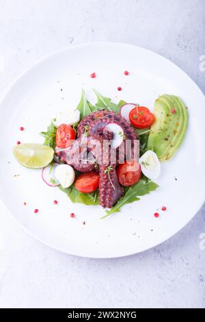 Warmer Salat mit Oktopus, Kirschtomaten, Avocado, Rucola, Wachteleiern, Rettich und Kalk auf einem weißen Teller. Traditionelle mediterrane Gerichte. Nahaufnahme, wh Stockfoto